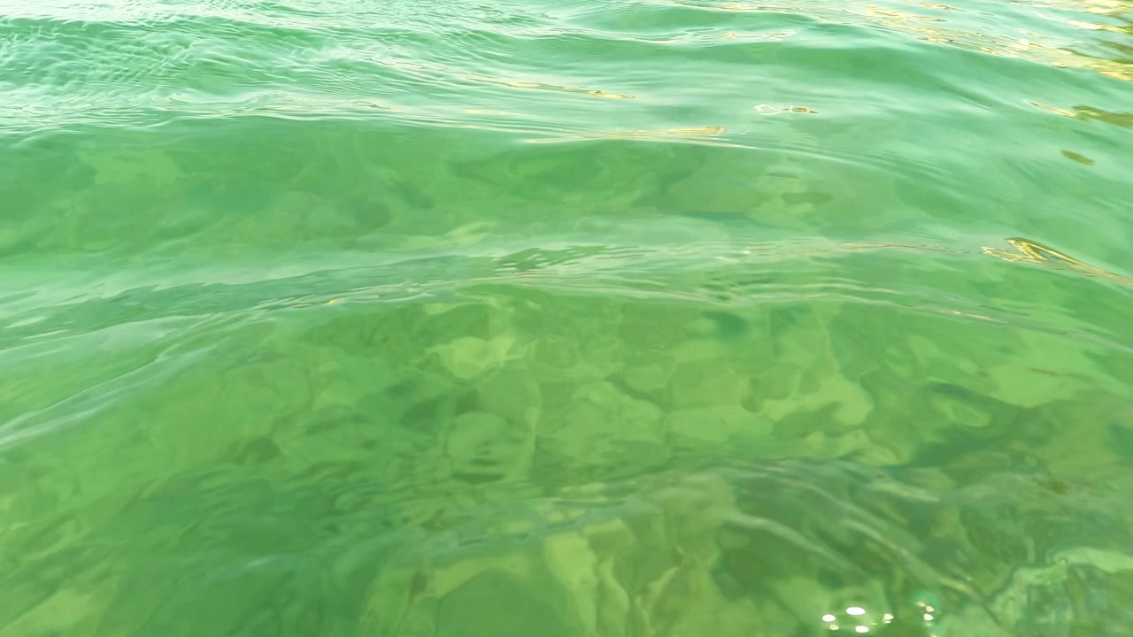 A shallow underwater view in Los Barriles shows the water surface brightening across the top of frame and a rocky seabed below, with no visible people.