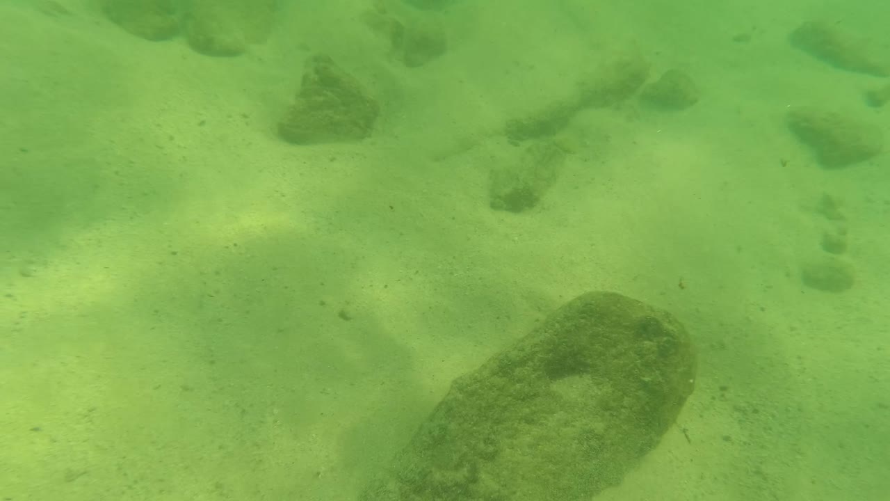 Sandy underwater bottom with a broad rock and smaller stones.