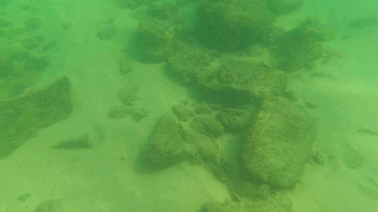 Larger rocks on sandy underwater floor in green water