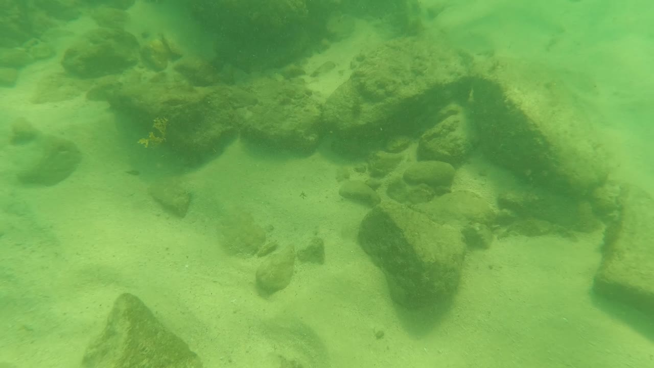 Underwater rocks and sand seen through green water