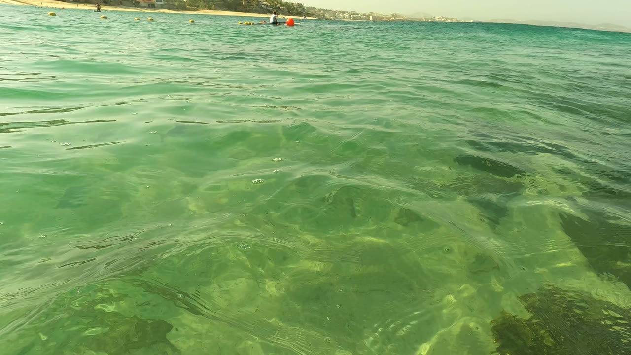 Rippling shallow water with distant buoys and shoreline at the horizon.