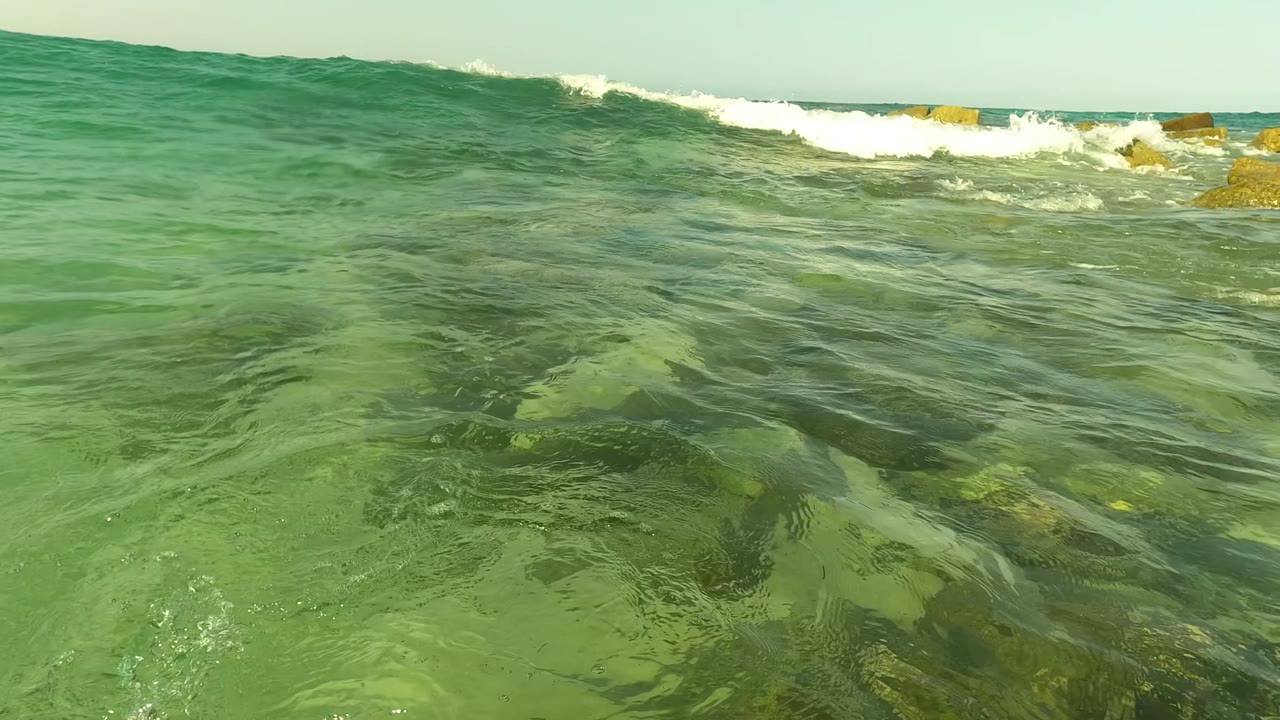 Green ocean surface with breaking wave and rocks near the horizon