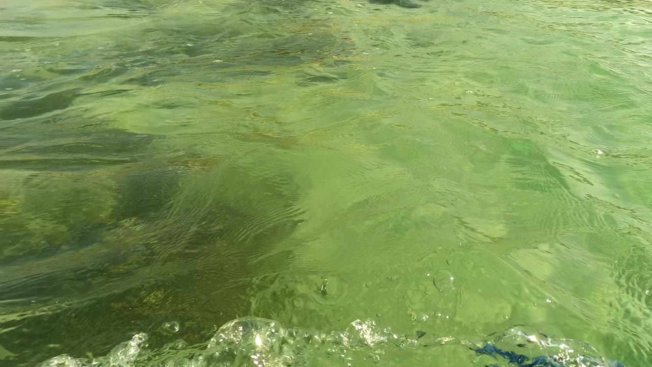 At Los Barriles, Baja California Sur, rippled green water dominates the frame, with submerged sand and darker rock shapes visible below the surface, with no visible people.