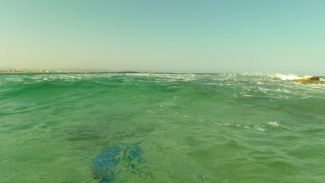 Green surface water fills the foreground near Los Barriles, with small whitecaps across the middle of the frame and no visible people.