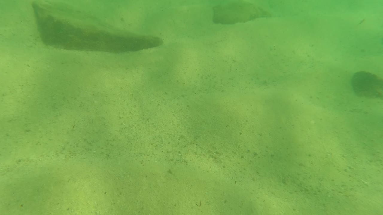 Sandy underwater bottom with rocks and soft light ripples