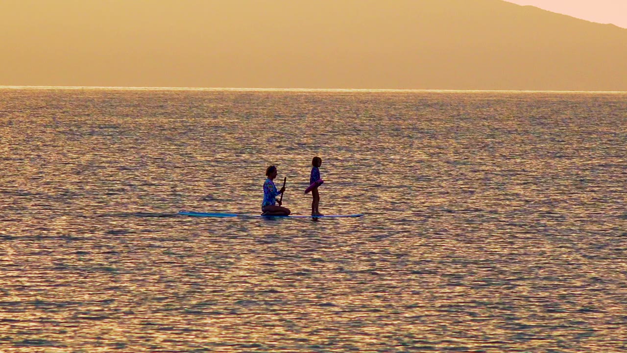 One person kneels and one stands on a paddleboard on golden water.