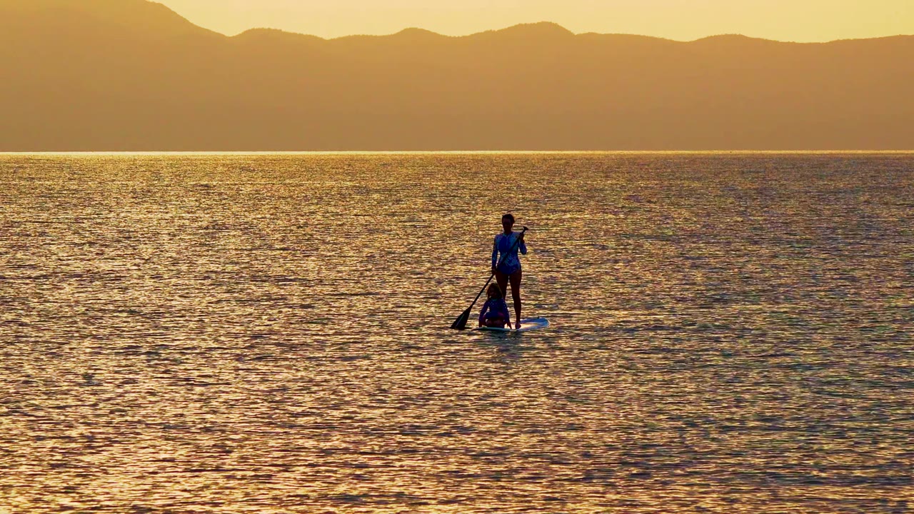 Paddleboarder farther across sunlit water near a mountain horizon