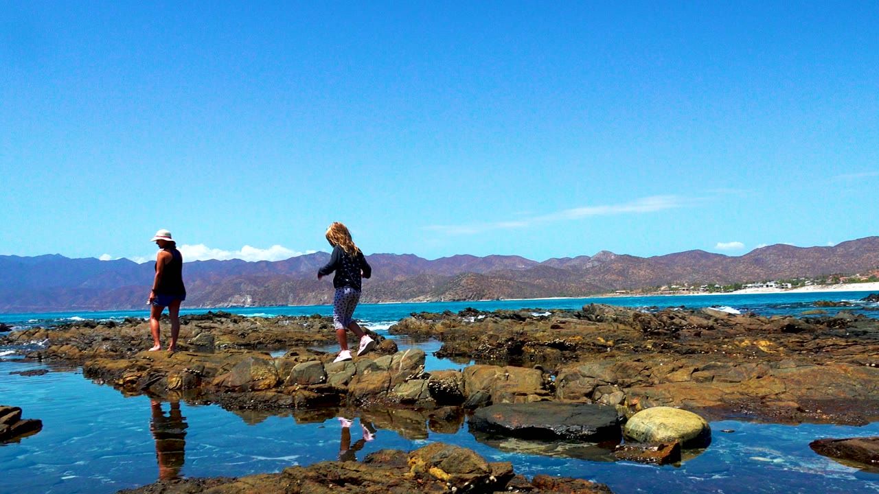 Man and girl on rocky shore beside reflective water