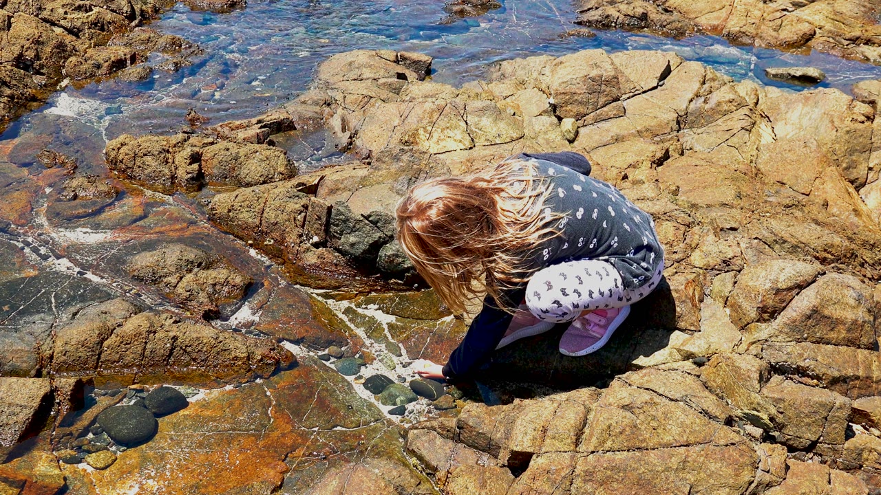 Girl leaning toward water on tan coastal rocks