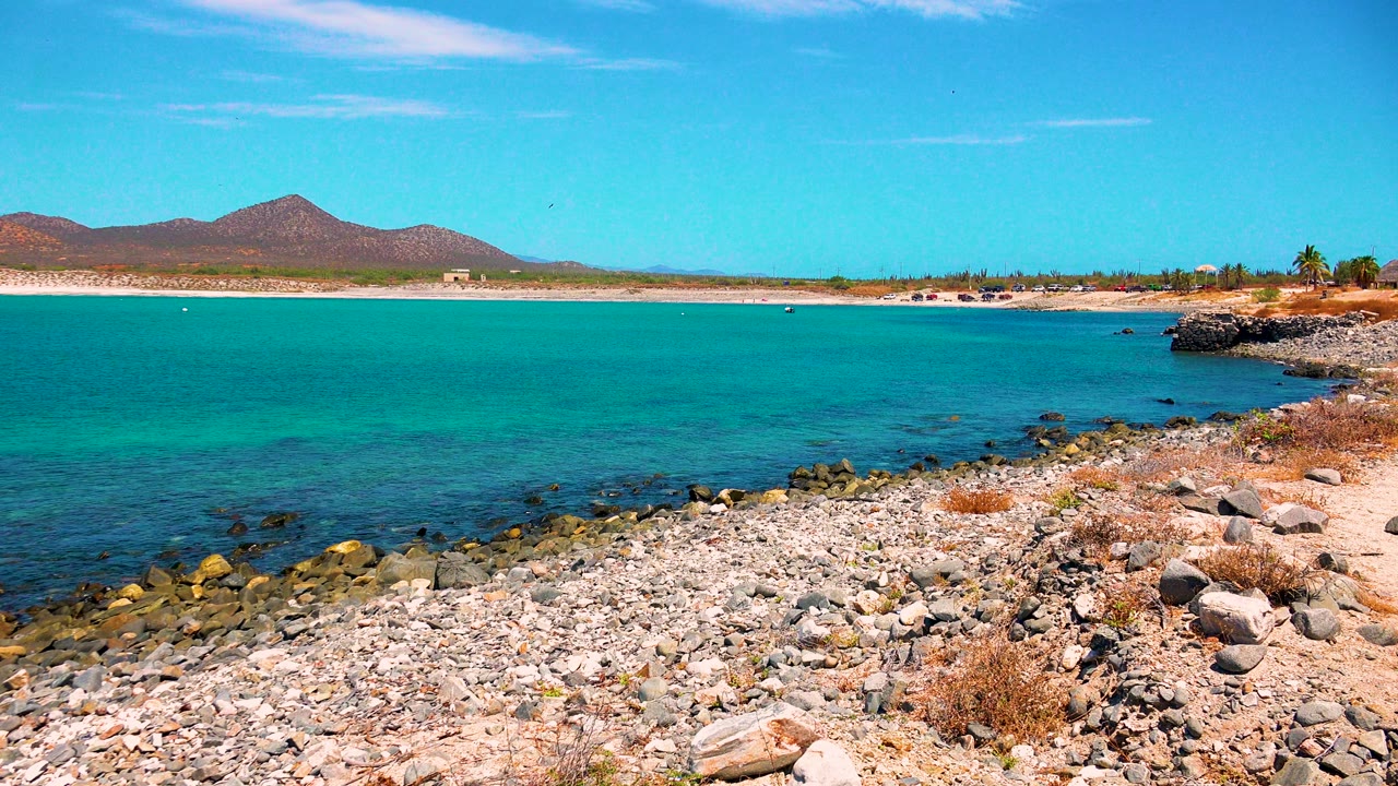 Rocky shoreline beside turquoise water with distant mountains
