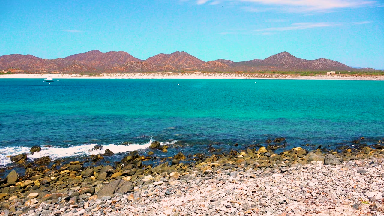 Turquoise ocean waves reaching a rocky shore with distant mountains