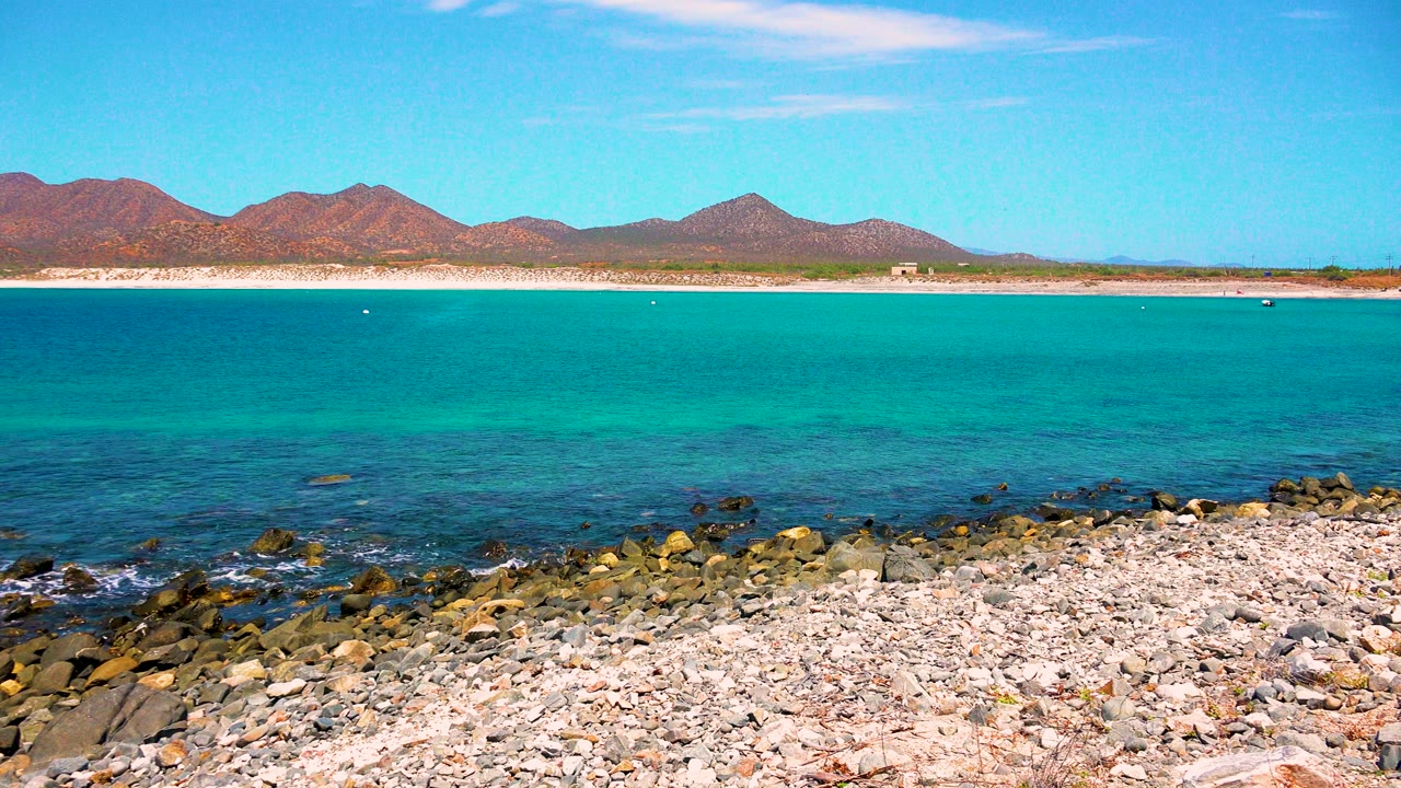 El Sargento La Ventana, Mexico shoreline frame with the waterline slightly farther across the rocks, turquoise sea in the center, distant mountains, and no visible people.