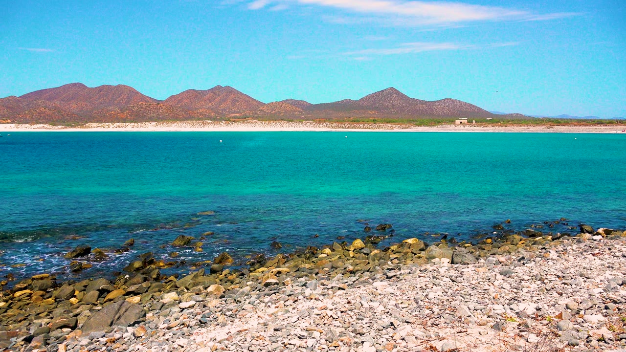 Pebble beach and calm turquoise sea below brown mountains