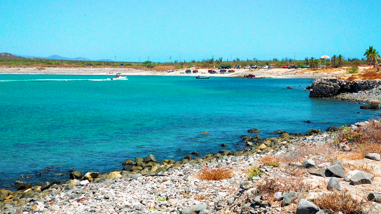 Rocky beach and turquoise bay with a boat near the far shore.