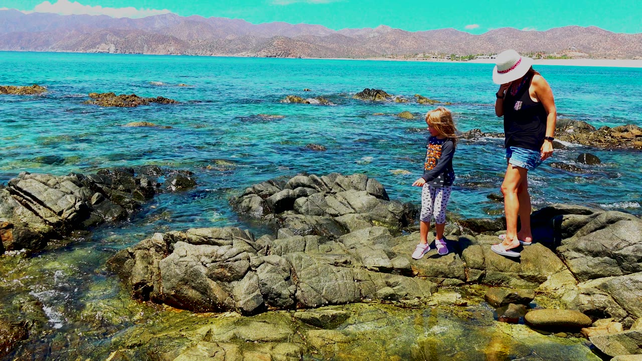 Girl and woman walking across rocks beside the ocean.