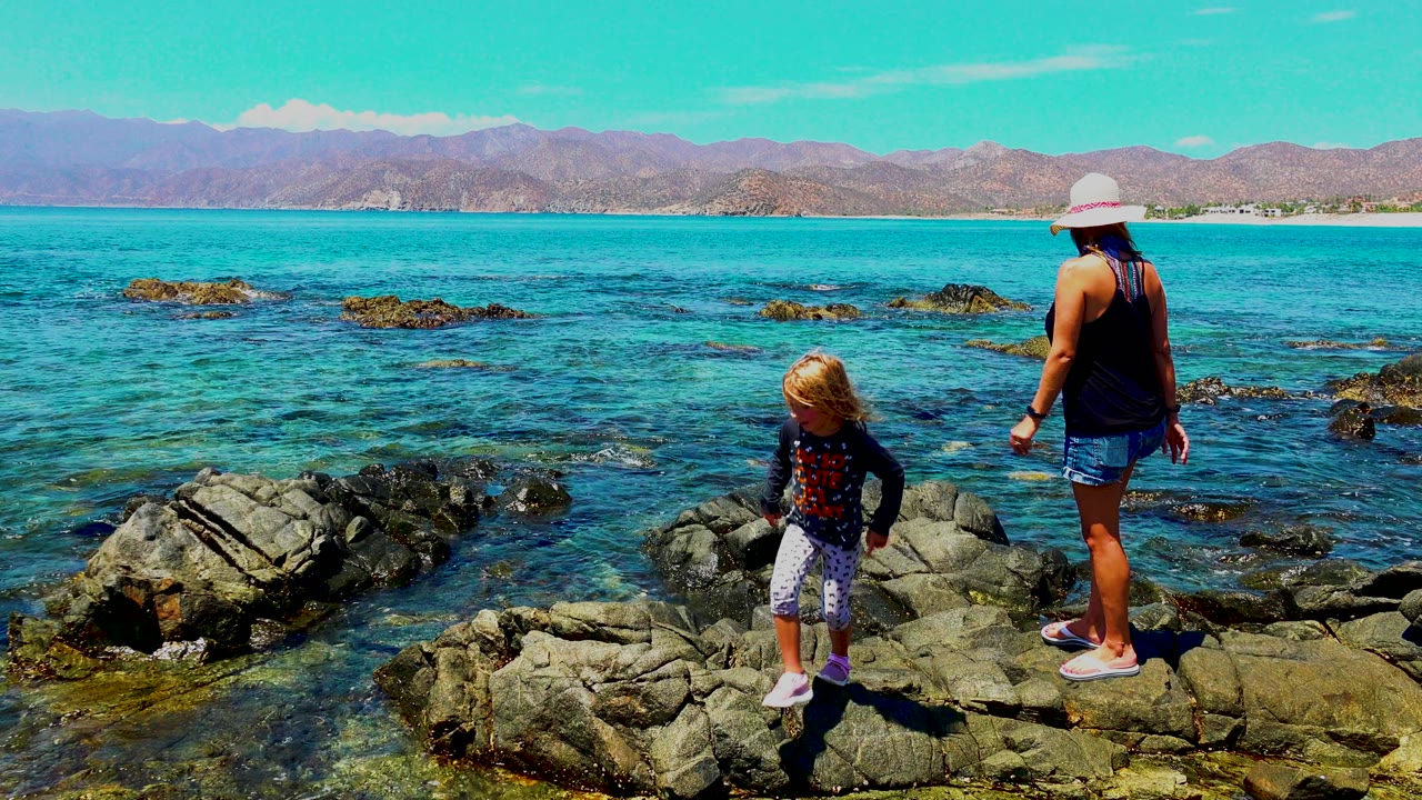 Child near foreground rocks while woman stands nearby at the shoreline