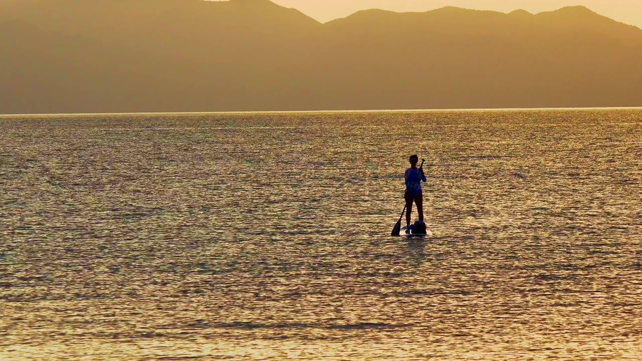 Paddleboarder centered on rippled sunset water with mountains behind.