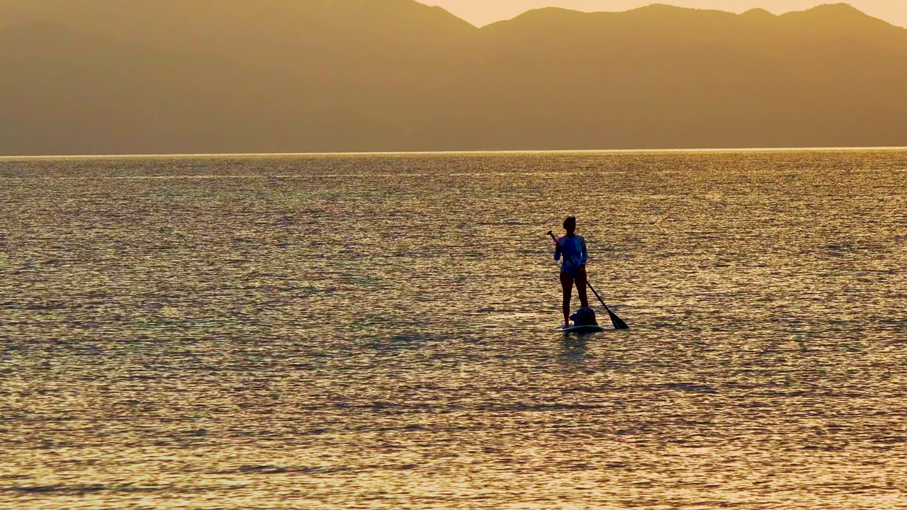 A silhouetted paddleboarder appears on the right side of the frame in La Ventana, Mexico, with the paddle angled down toward the rippled water.