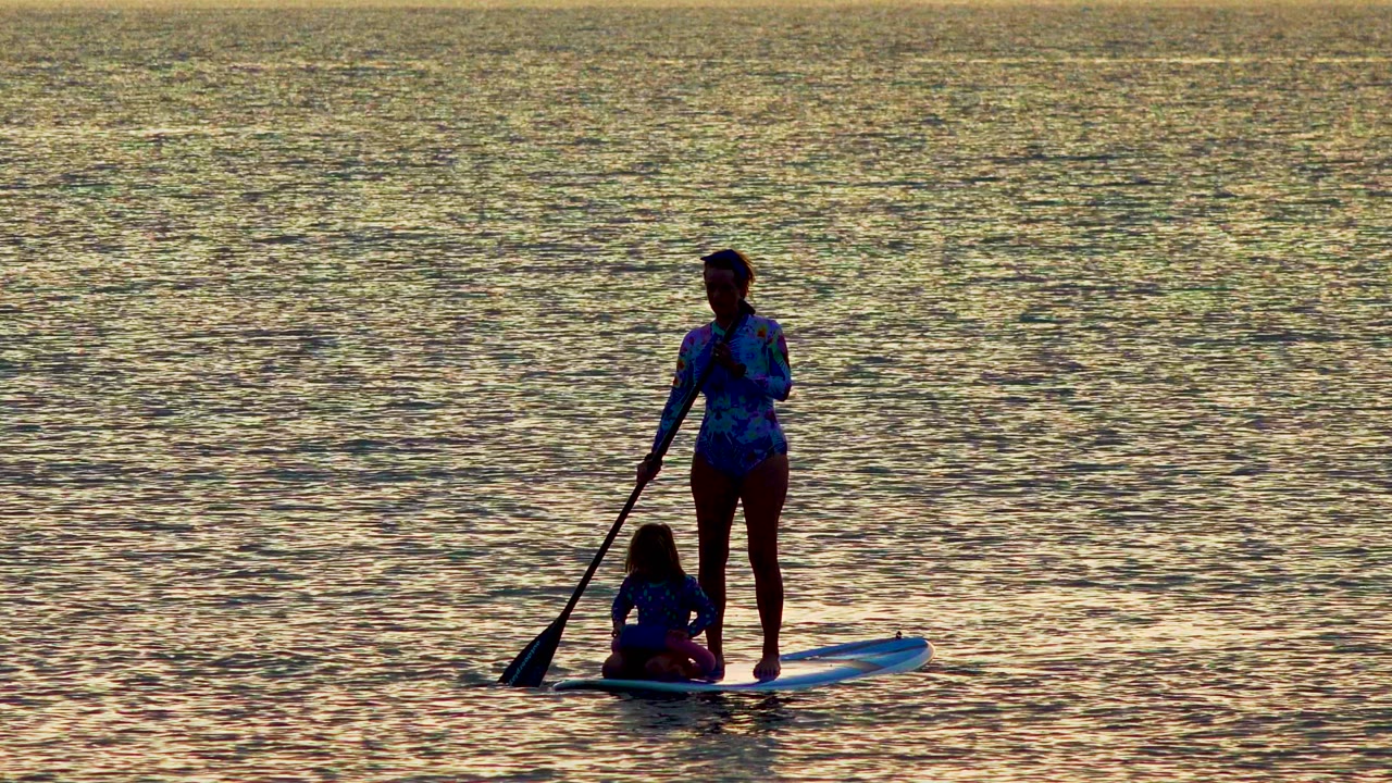 Paddle blade touches water beside a board carrying two people.