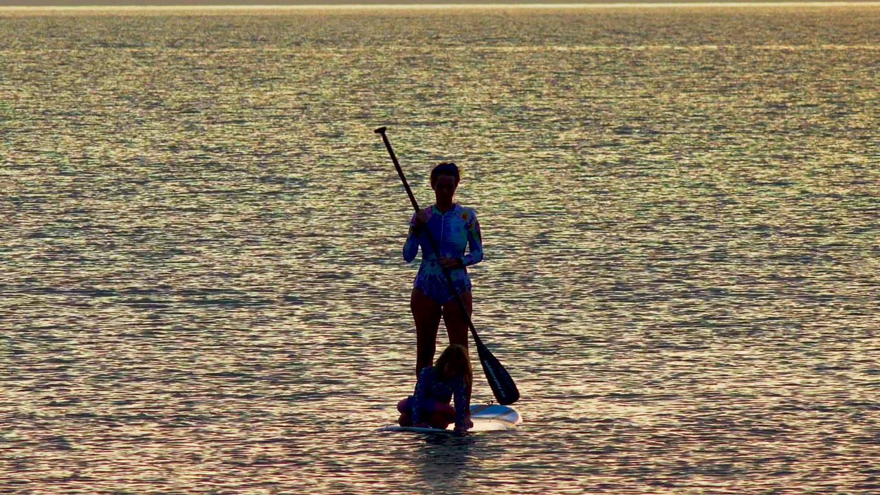 Standing paddler and seated rider on reflective water