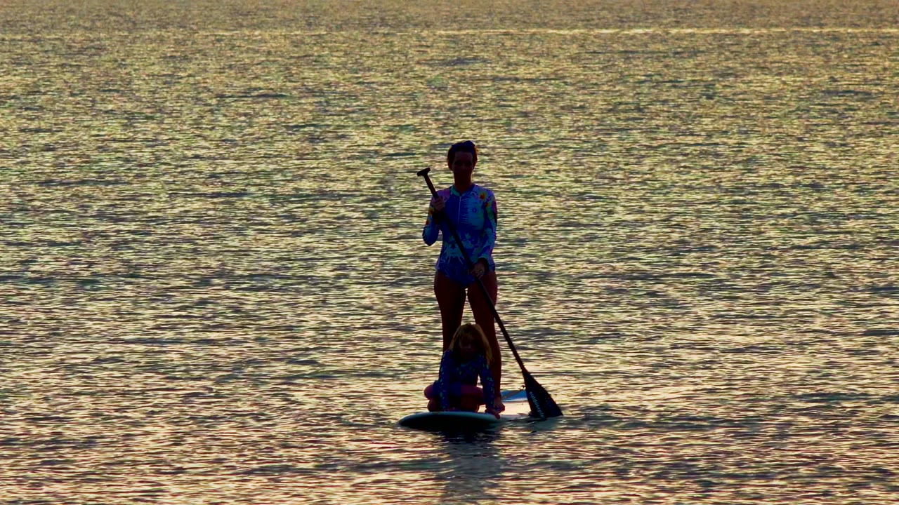 Two silhouetted paddleboarders in La Ventana, Mexico appear near the right side of the frame, with the standing person holding the paddle across the body.