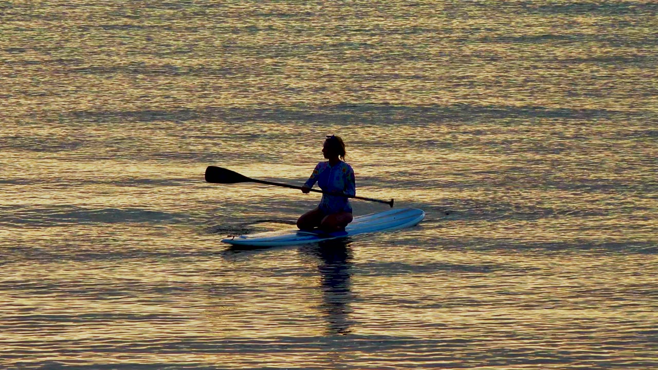 Paddleboarder holding a paddle across calm golden water.