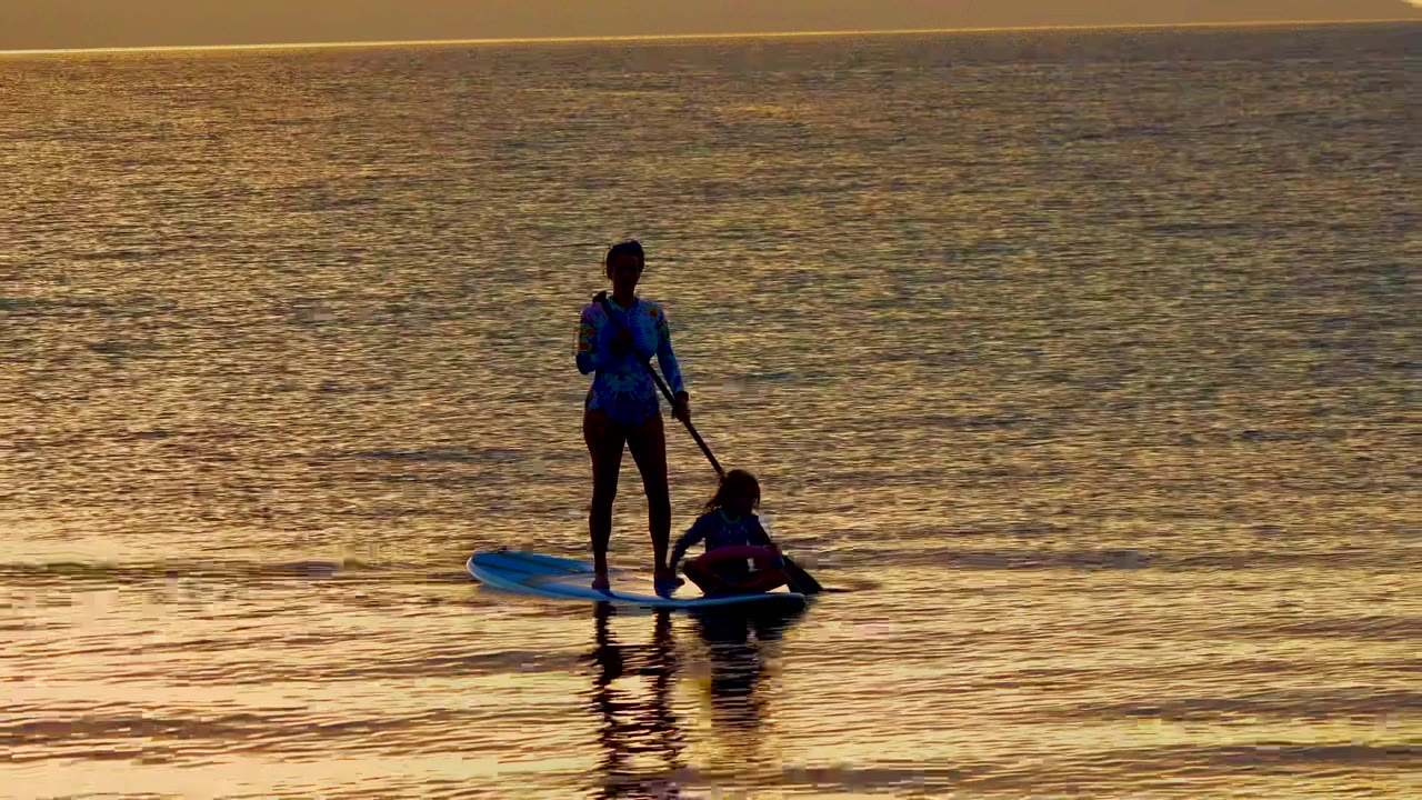 At 0:00 in El Sargento, Mexico, a standing paddleboarder holds a paddle while a second person sits low near the board edge in gold reflected water.
