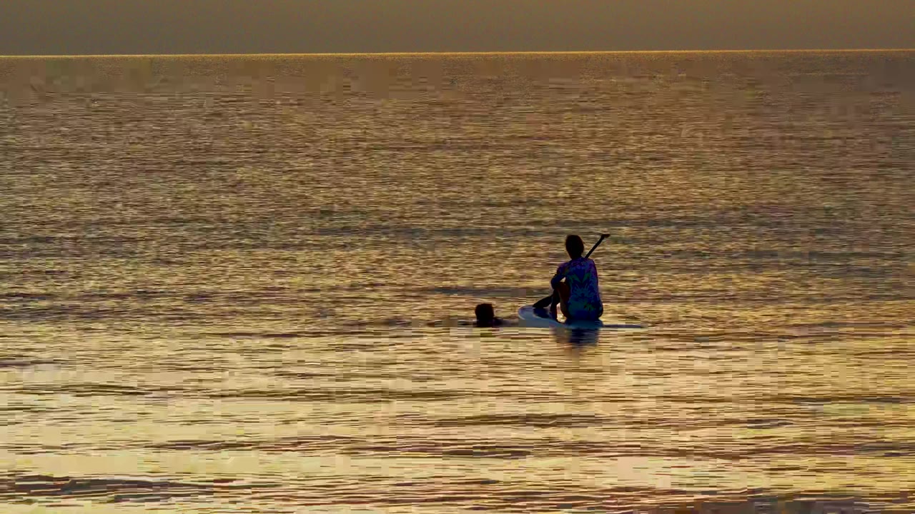 Silhouetted kayaker sits near a swimmer’s head on golden ocean water in El Sargento La Ventana, Mexico, with the horizon high in the frame.