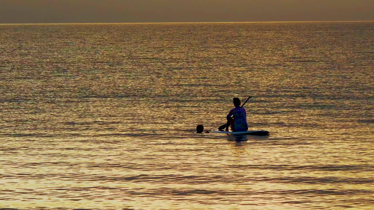 Kayaker paddling beside a swimmer on reflective water.