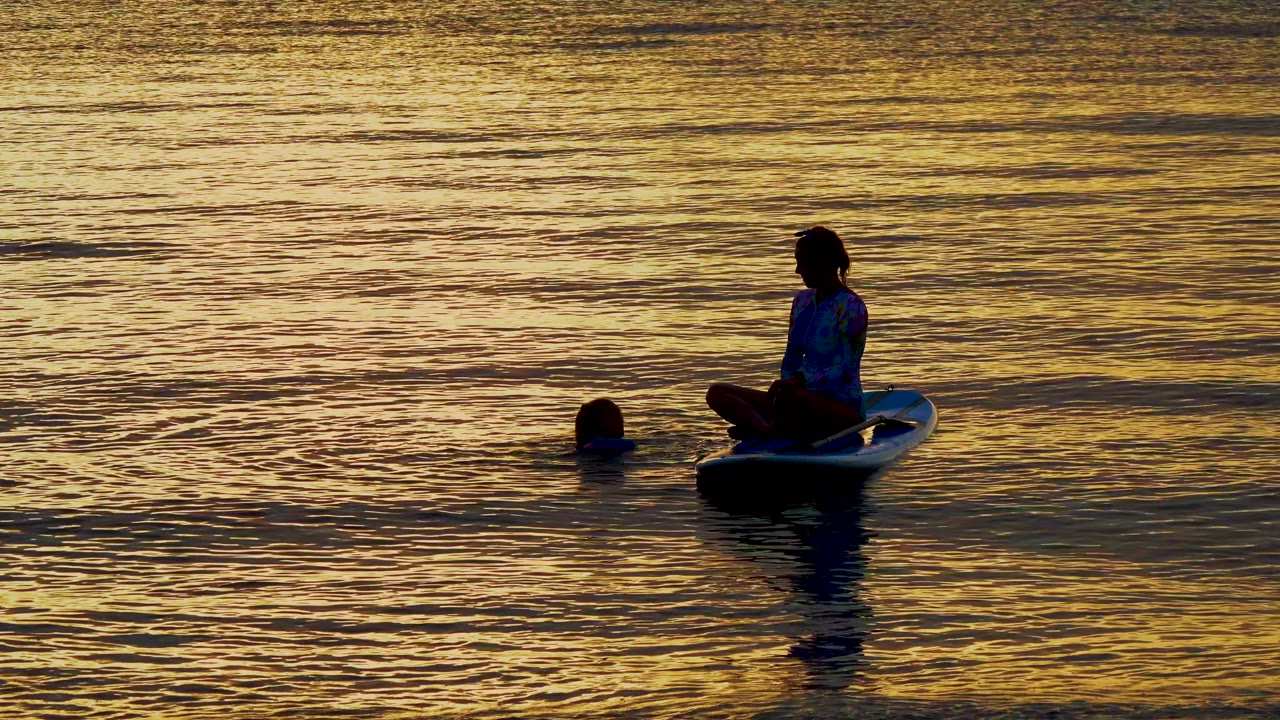 At El Sargento, Mexico, the swimmer floats low in the water while the seated person on the board is silhouetted against a wide field of amber ripples.