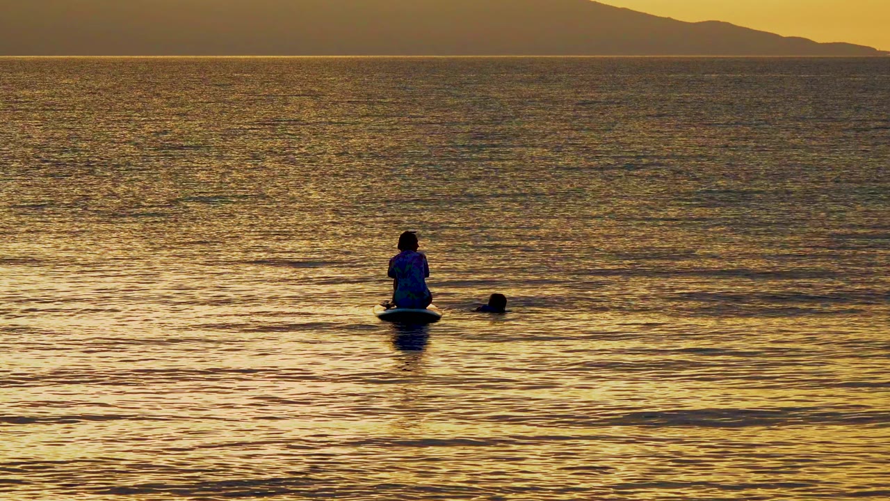 Paddleboarder centered on calm golden water with swimmer nearby
