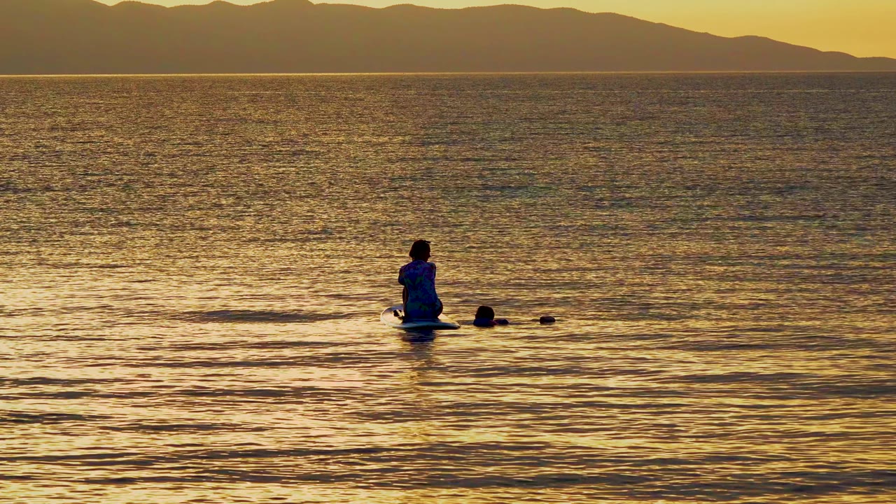 At 0:00 in El Sargento, Mexico, a person sits on a paddleboard near another small figure in the water, with golden reflections and dark mountains on the horizon.