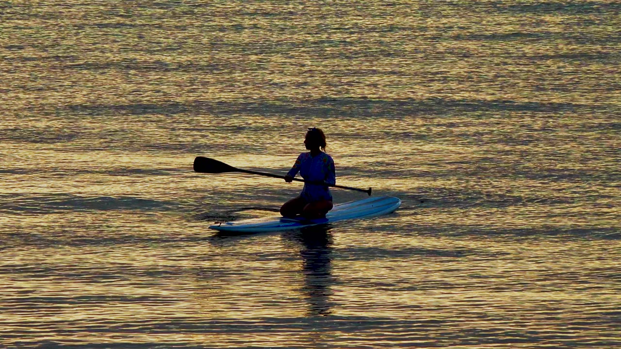 Paddleboarder raises a paddle over calm reflective water.