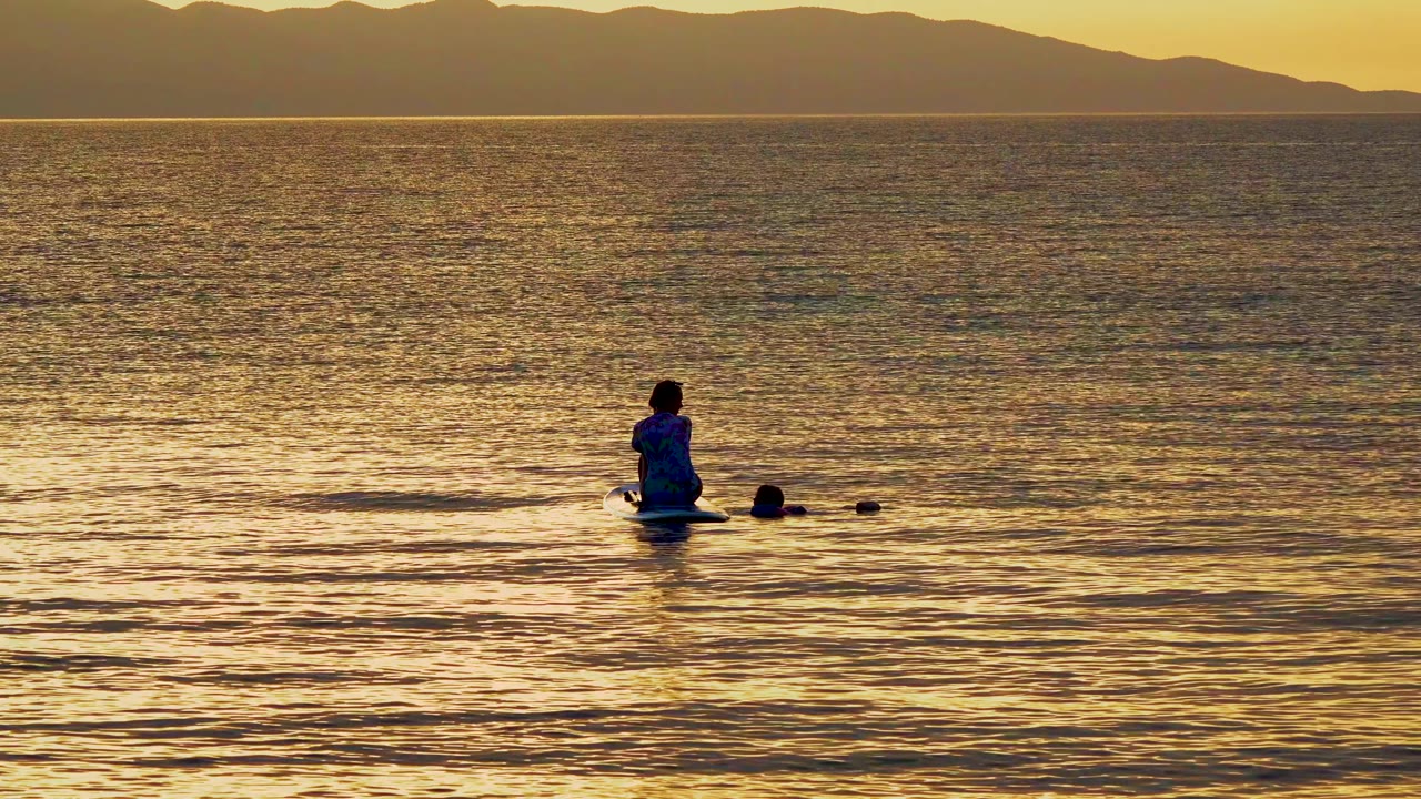 At 0:00 in El Sargento, Mexico, a small silhouetted person sits on a paddleboard beside a dog in calm golden water with mountains on the horizon.