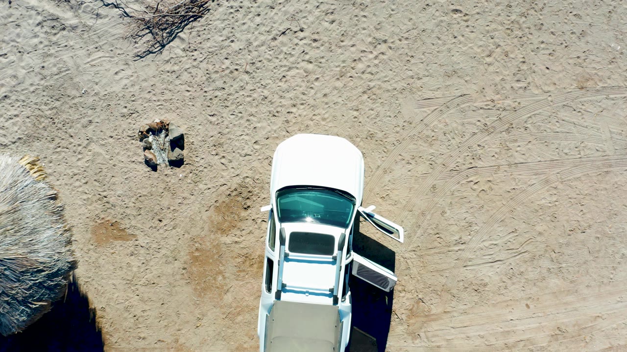 At 0:00 in Juncalito, Baja California Sur, an overhead view shows a white car partly in frame with its driver's door open and a person on the sand above it.