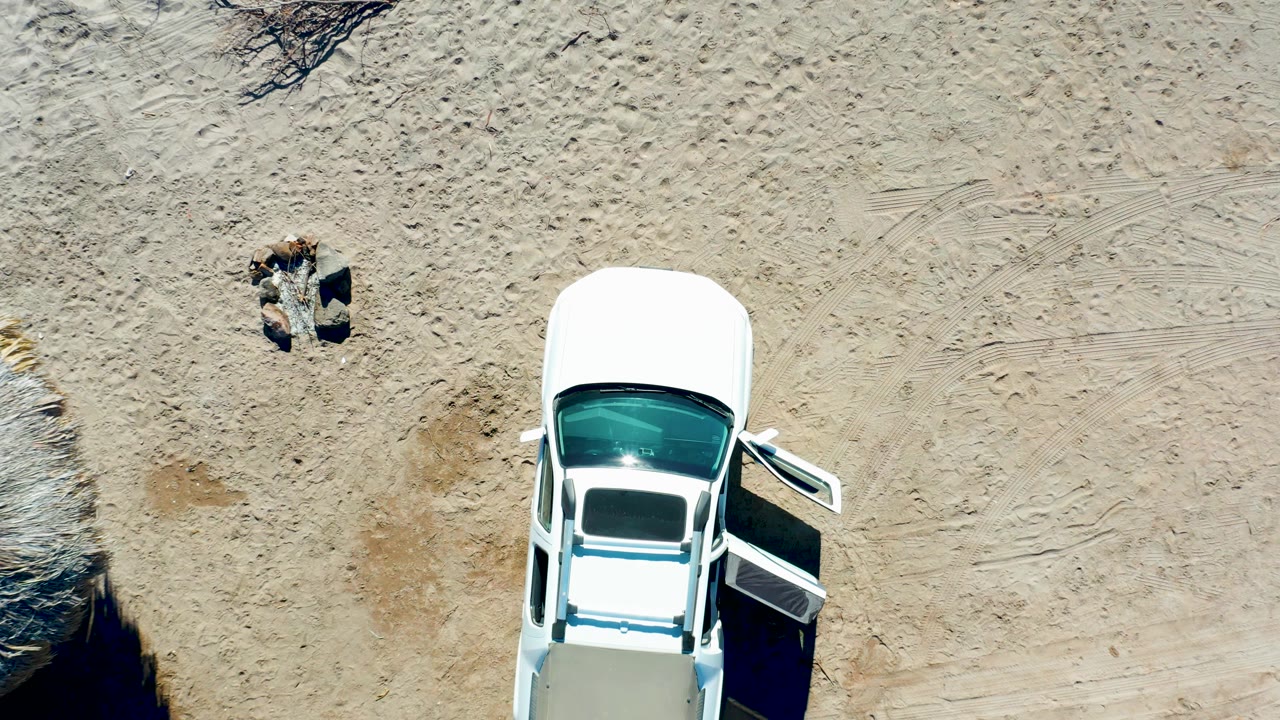White car with open door below a person lying on sandy ground.