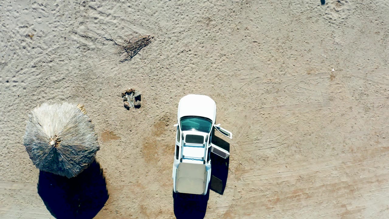 White car with open door beside a beach umbrella on sandy ground