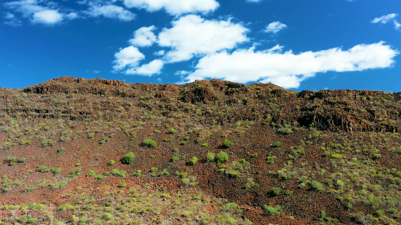 Fourth frame shows the wide San Javier hillside with red soil, brown rock, scattered green bushes, bright overhead cloud cover, and no visible people.