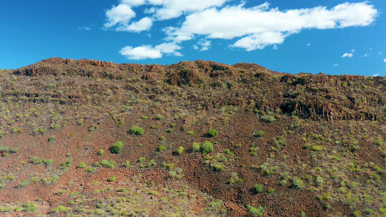 At 0:01, the San Javier hillside ridge stretches across the frame with scattered green shrubs, reddish rock, a large white cloud band, and no visible people.