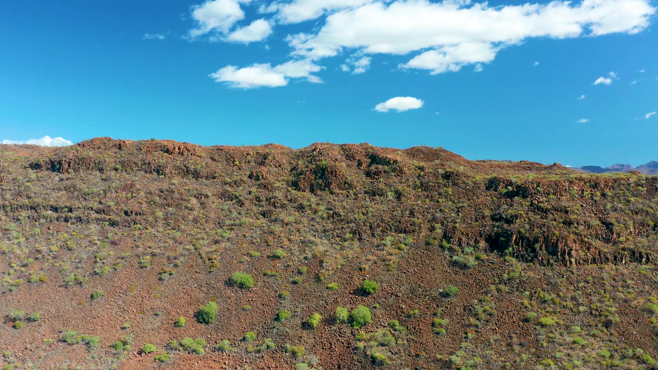 Dry rocky slope with green shrubs beneath a broad blue sky.