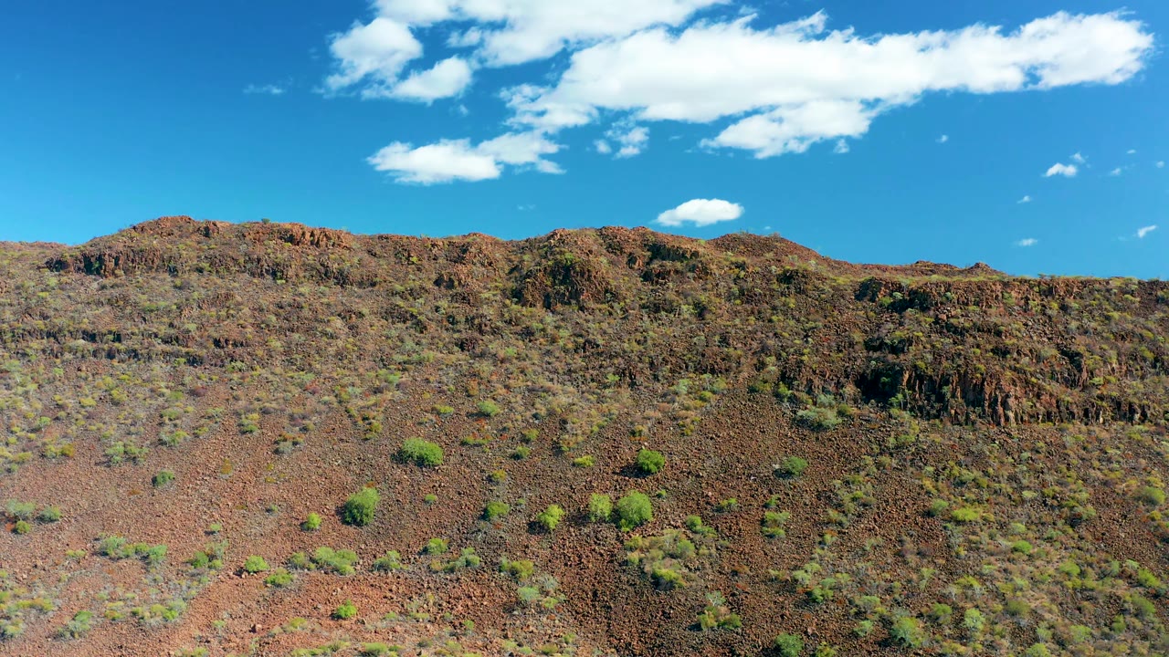 Rocky desert slope with sparse shrubs and a bright clouded sky.