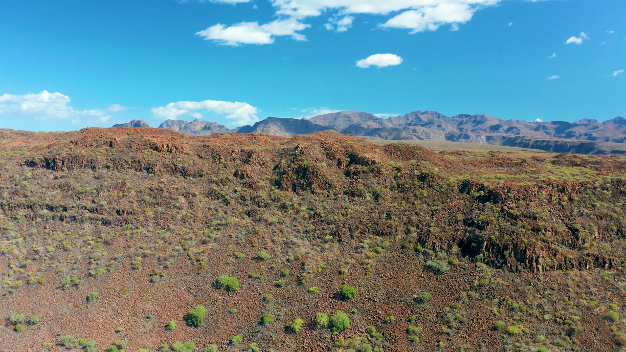 Aerial view of red rock desert and low mountains under clear sky
