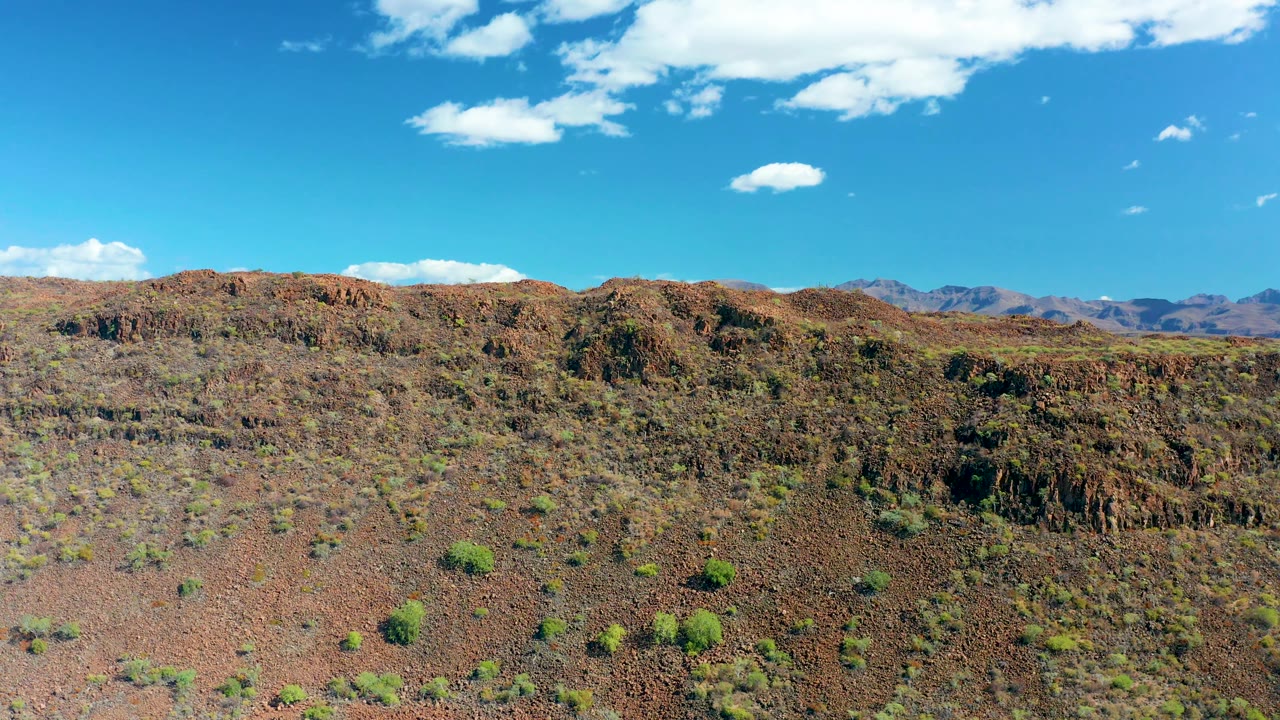 Rocky arid slope with sparse shrubs and distant mountain ridge.