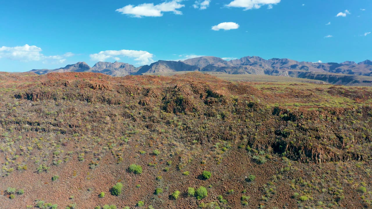 Second frame shows the San Javier desert plateau with red-brown rocky ground, scattered shrubs, layered ridges, distant mountains, and no visible people.