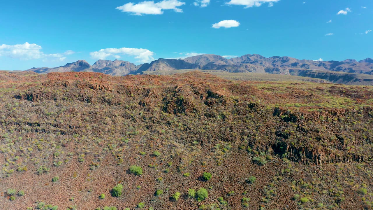 Third frame presents the San Javier arid landscape with red rock foreground, sparse green shrubs, a mountain range in the background, bright sky, and no visible people.