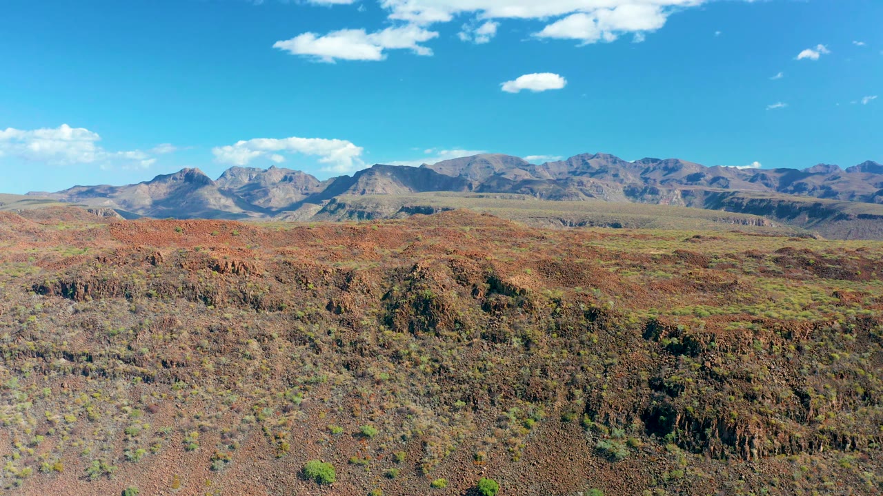 Fourth frame presents rocky desert basin terrain in San Javier, Baja California Sur, with low green shrubs, a continuous mountain line, bright blue sky, and no visible people.