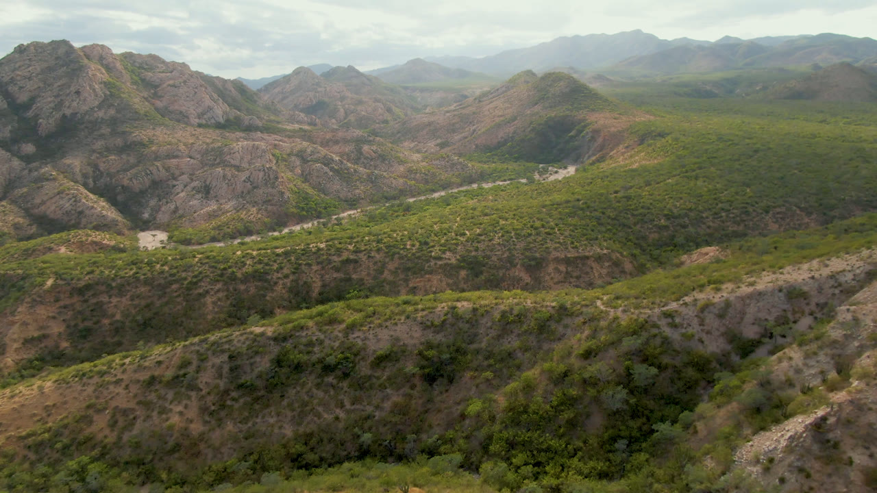 Aerial mountain landscape with arid slopes, green brush, and a road crossing the middle.