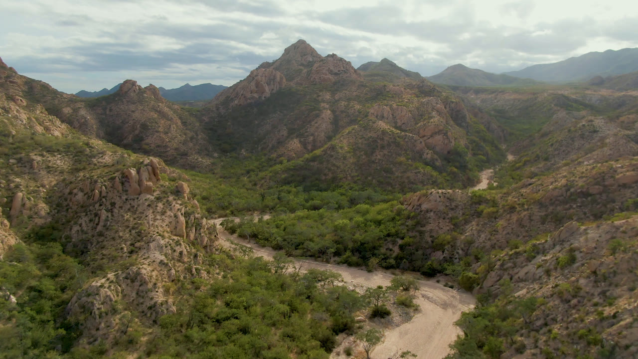 Wide aerial view of a dirt road winding below rocky desert hills.