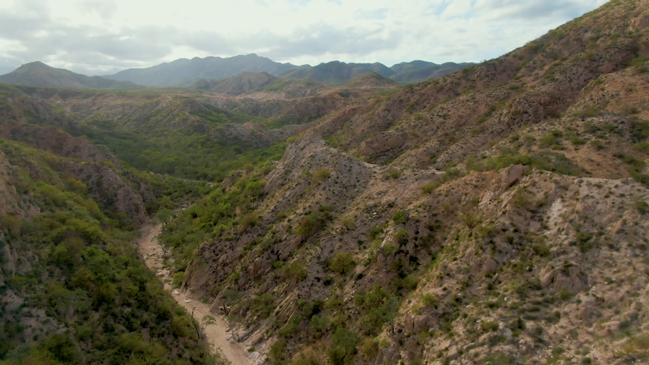 Aerial view of rocky mountains and a green valley under cloudy sky.