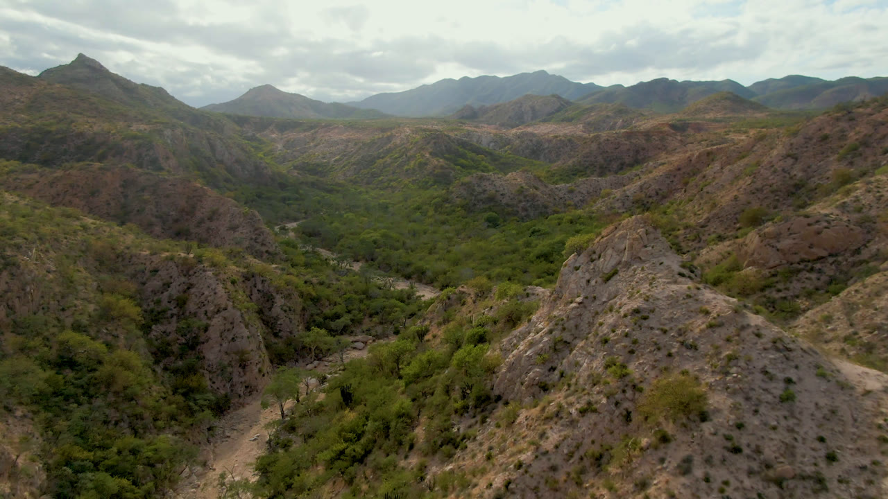 Aerial view of rocky hills and a green valley under clouds.